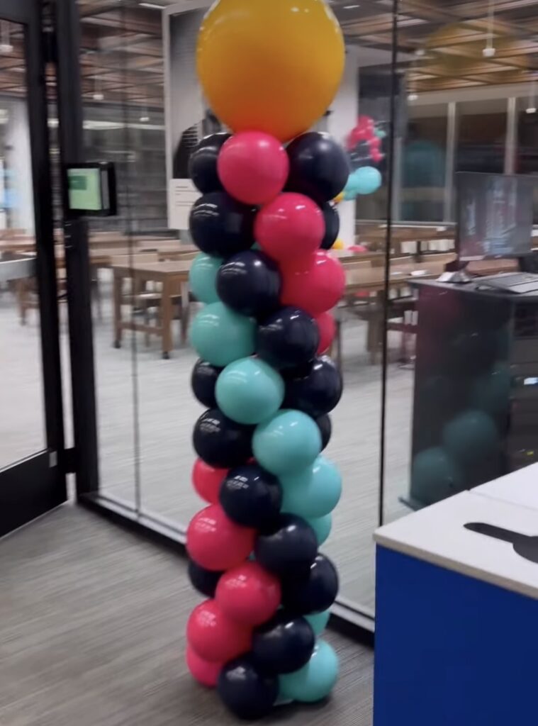 A colorful and creative balloon tower arrangement in front of the door to a business